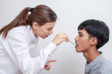 Beautiful young woman dentist in uniform using dental mirror to examine the teeth in the patient's mouth.