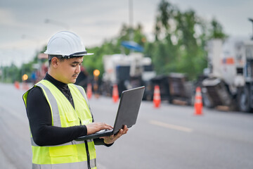 Young Asian engineer checking a rural road project online after work at a road construction machine.
