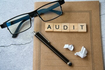 Audit word written in wooden letters on a notepad, glasses, and a pen