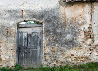 Weathered grey wooden door in old dilapidated stone wall.