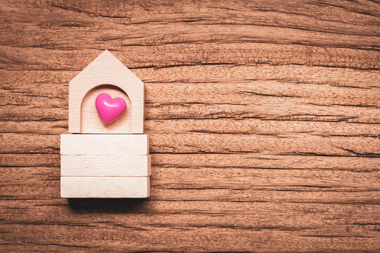 Top view of wooden house and pink heart put on the wooden block on old vintage wood in the office, The buying a new real estate as a gift to family or the one loved concept.