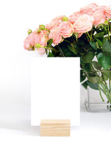 Blank card in a wooden stand with roses in a vase in the background