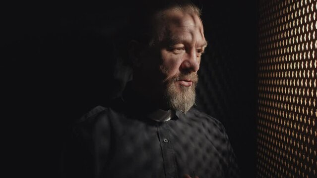 Medium close-up tilt up shot of Catholic priest having conversation with penitent in confessional