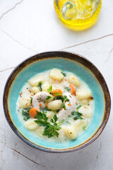 Creamy soup with chicken and potato gnocchi in a turquoise bowl, vertical shot on a white granite background, selective focus
