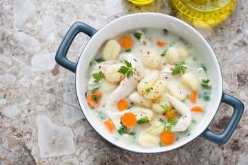 Serving pan with creamy chicken gnocchi soup, horizontal shot on a light-brown granite background, high angle view