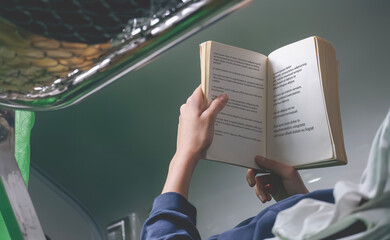 Focus at Hand of female passenger reading a book while resting on the top seat of sleeper train while travelling, text in book page is lorem ipsum