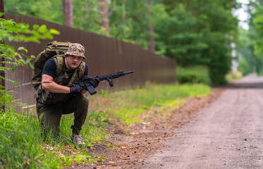 A man in military uniform peeks out from behind the bushes.