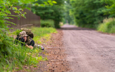 A man in military uniform takes aim from a prone position
