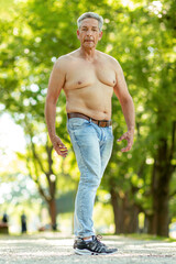 Portrait of a shirtless best ager man posing in a park in summer outdoors