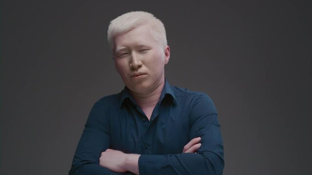 Portrait of an Asian albino guy. Eastern man with a genetic mutation of pigment, white hair. The arms are crossed on the chest. The male is wearing a dark shirt in the studio. Abnormal deviations