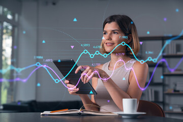 Smiling businesswoman in casual wear holding tablet device touching it at office workplace. Concept of distant work, business education, information technology. Forex graph and chart hologram