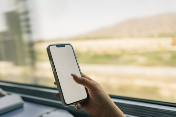 Woman's hand holding mobile phone on a high speed train ride. Unrecognizable young girl using phone technology while traveling on high speed train for leisure or business.