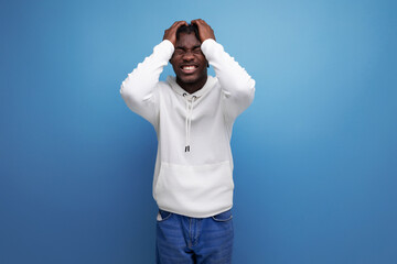 Naklejka premium cute african young brunette male in white sweater smiling broadly on blue background