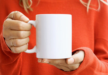 Girl is holding white 11 oz mug in hands with orange sweater. Blank ceramic cup