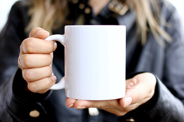 Girl is holding white mug in hands with black leather jacket.  Blank 11 oz ceramic cup