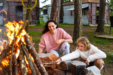 Mother with her daughters spending time together, kindle a fire and throw sticks