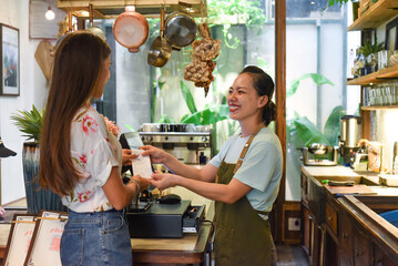 Young Vietnamese waitress working with check out machine and customers in cafe
