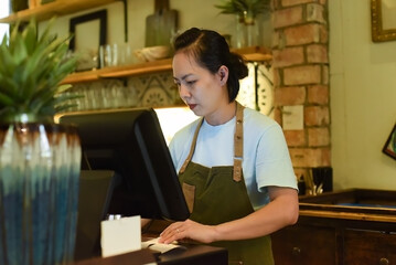 Fototapeta premium Young Vietnamese waitress working with check out machine in cafe 