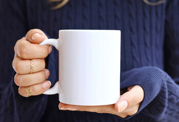 person holding a cup of coffee with navy blue sweater. Blank ceramic cup
