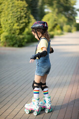 Cute little girl in protective equipment and rollers stands on walkway in park outdoor. Summer...