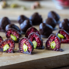 Pistachio filled chocolate covered raspberries on a wooden board.
