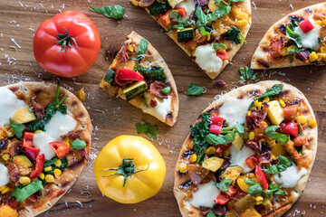 Homemade summer garden pizzas with heirloom tomatoes on a wooden board.