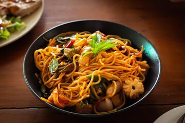 Close up Kee Mao spaghetti, squid, black plate on brown wooden table, this menu originates from the fusion of local Thai food and the food of the Chinese immigrants in Thailand.