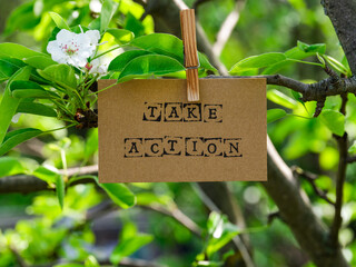 Piece of cardboard with the words Take Action on it hanging on a pear tree branch with blossoms and...