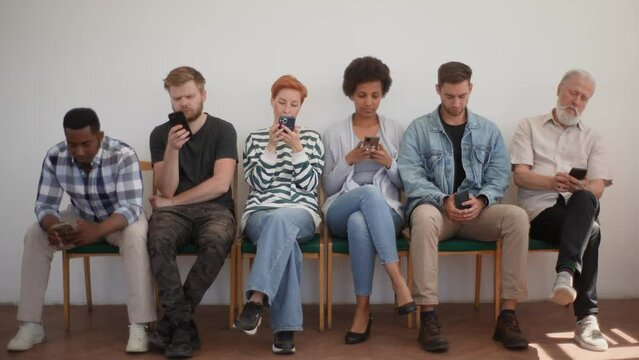 Portrait of multicultural and different ages professional business people for vacancy in casual clothes sitting on chairs in row using mobile phones, while waiting job interview on white background