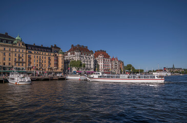Fototapeta na wymiar Sightseeing and passenger ferries at the pier in the bay Nybroviken, background hotels and office buildings, a sunny summer evening in Stockholm