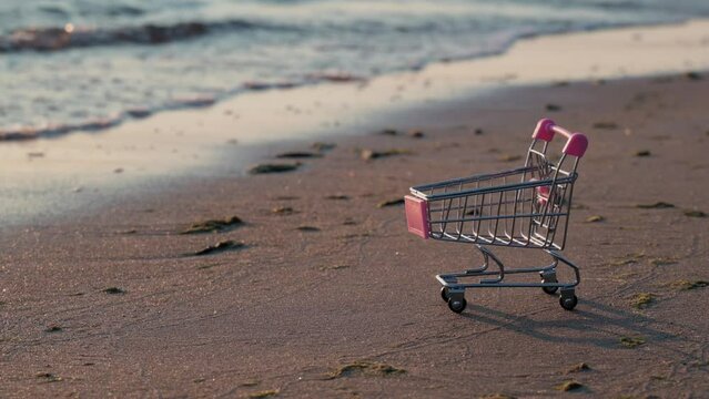 An empty miniature shopping basket, on the shore washed by water. Summer sale concept.