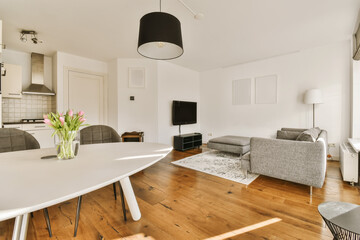 Fototapeta na wymiar a living room with wood flooring and white walls, including a large dining table surrounded by two grey chairs