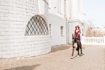 A photo of a woman and her Great Dane walking through a town, taking in the sights and sounds of...