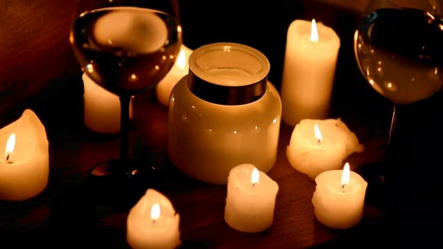 A lot of candles are burning in the dark, white wine is splashing in two glasses. Romantic candlelit dinner