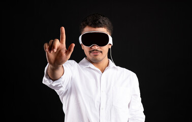 Naklejka premium Metaverse concept. Modern latin man in vision pro vr glasses, trying to touch something with finger on black background