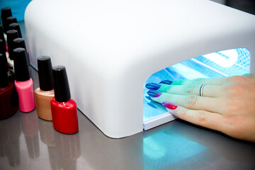 Woman getting professional manicure in beauty salon, master applies gel polish on nails and dry in...