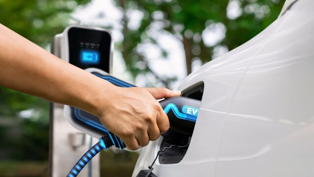 Hand insert EV charger and recharge electric car from charging station on nature and travel concept background. Technological advancement of alternative energy sustainability and EV car. Peruse