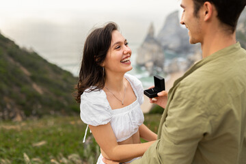 Young loving man with engagement ring making proposal to happy woman on mountains, having romantic...