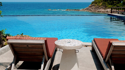 Fototapeta premium Two beach chairs and a cocktail table near a swimming pool on a sunny day. Summer vacation. Concept of relaxation and leisure.