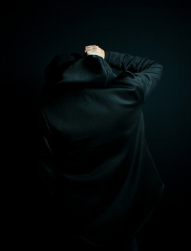 Man standing alone in the dark wearing a black hoodie and hat