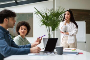 Serious Asian Lady Listening Employee During Team Meeting At Office