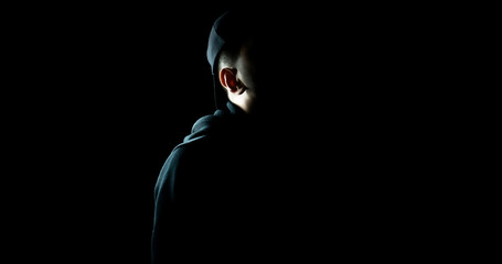 Man standing alone in the dark wearing a black hoodie and hat - obrazy, fototapety, plakaty