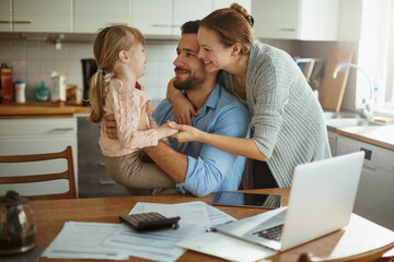 Young family hugging in the kitchen while going over their bills in the morning