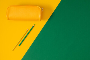 Back to school concept. Yellow school pencil case with filling school stationery, notebook, pens, pencils. School accessories on green background. Flat lay, top view, copy space