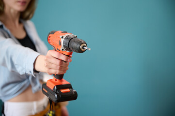 Young female worker with tool belt holding an electric screwdriver in hands isolated on background. Pretty caucasian female with tools planning new project. Portrait in studio. Crop view.