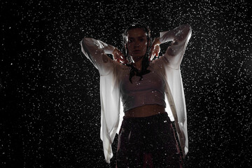 Dancing in the rain. A young woman in wet clothes dancing among water droplets, photo in the aqua...