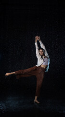 Dancing in the rain. A young woman in wet clothes dancing among water droplets, photo in the aqua studio - 624141278