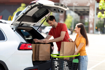 Couple buying food in grocery store, packing purchases in car