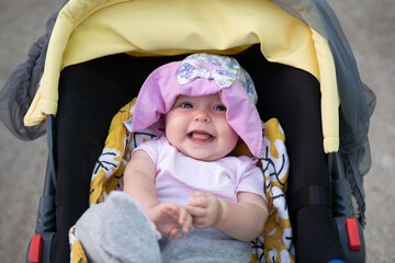 Smiling baby girl walking on the stroller in warm summer day. Childhood and motherhood concept.