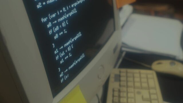 Selective focus close-up of old computer monitor with code on screen on table in 90s office